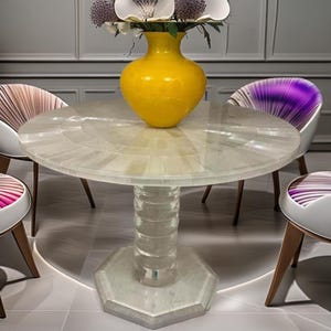 Può includere: Tavolo da pranzo rotondo e chiaro con base decorativa. Un vaso giallo con fiori è posto sul tavolo. Il tavolo è circondato da sedie con sedute decorate e gambe in legno. Diametro del tavolo: circa 120 cm.