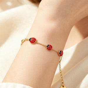 Peut inclure: Un bracelet à chaîne dorée orné de trois petites breloques en forme de coccinelle avec des ailes en émail rouge et des points noirs. Le bracelet comprend une fine chaîne à maillons, un fermoir mousqueton et une petite breloque ronde dorée.