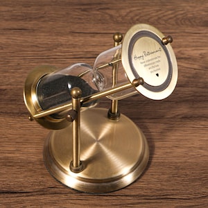 Può includere: Una clessidra in stile antico con finitura in ottone. La camera di vetro contiene sabbia nera. La parte superiore della clessidra riporta la scritta "Happy Retirement" e un messaggio. Un regalo premuroso.