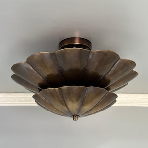 Può includere: Una plafoniera a due livelli con finitura in bronzo scuro. L'apparecchio presenta un design smerlato a forma di petalo con due paralumi sovrapposti a forma di ciotola che si allargano verso l'esterno, fissati da un terminale centrale sul fondo.