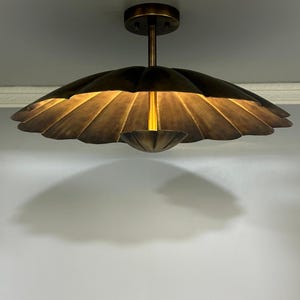 Peut inclure: Un plafonnier en bronze avec un abat-jour en forme de pétale. Le luminaire a une tige centrale et un petit bol orienté vers le bas. La lumière est allumée, dégageant une lueur chaleureuse.