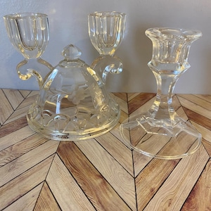 May include: Clear glass candle holders and a covered dish. The candle holders include a double-arm design and a single candlestick. The covered dish has a floral design etched on the lid.