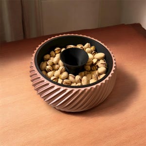 May include: A light brown serving bowl with a spiral design. The bowl has a black interior and a central black cup, filled with pistachios. The bowl is designed for serving snacks, a stylish addition to any table setting.