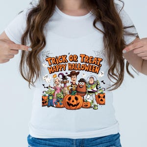 Puede incluir: Camiseta blanca con un diseño de Halloween. El diseño incluye personajes de dibujos animados, calabazas, fantasmas y el texto "Trick or Treat, Happy Halloween" en naranja y negro. La camiseta tiene cuello redondo.