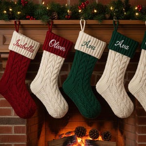 May include: A selection of cable-knit Christmas stockings in red, cream, and green, each with a contrasting cuff and a name embroidered in cursive. The stockings are suspended above a fireplace, decorated with festive greenery.