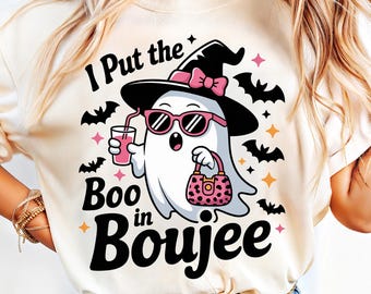 May include: Cream-colored t-shirt featuring a cartoon ghost wearing sunglasses, a witch hat with a pink bow, and carrying a pink purse. The text "I Put the Boo in Boujee" is printed above and below the ghost, with bat and star graphics.