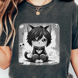 May include: Dark gray t-shirt featuring a black and white anime-style cat character with large eyes, wearing a hoodie. The graphic includes skulls and other decorative elements. The shirt is a casual wear item.