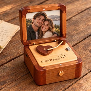 May include: A wooden music box with a hinged lid displaying a photograph of a couple. The box features a heart-shaped wooden tone arm, a speaker grille, and the engraved text Emma heart James. A small gold heart-shaped latch secures the front.
