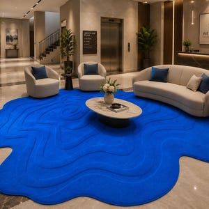 May include: A large, vibrant blue area rug with an irregular, organic, cloud-like shape and a textured, wavy, topographical pattern. The rug is positioned on a polished light-colored floor in a lobby setting, featuring raised, flowing lines.