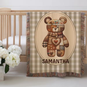 Pode incluir: Um cobertor tecido bege e castanho com um desenho de urso de pelúcia. O urso tem um design de patchwork com um coração e detalhes florais. O cobertor tem um fundo xadrez e o nome "SAMANTHA" está impresso na parte inferior.
