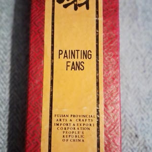 May include: A rectangular box with a red patterned exterior and a yellow label. The label reads "PAINTING FANS" in English and features Chinese characters. The text "FUJIAN PROVINCIAL ARTS & CRAFTS" is also visible.