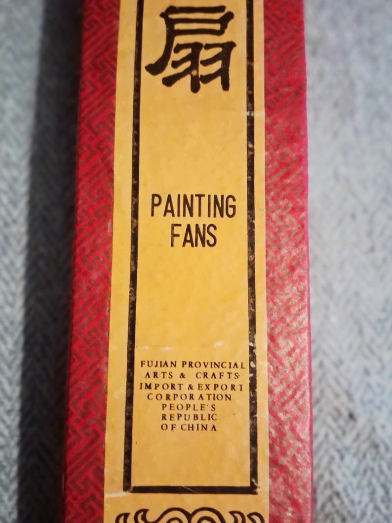 May include: A rectangular box with a red patterned exterior and a yellow label. The label reads "PAINTING FANS" in English and features Chinese characters. The text "FUJIAN PROVINCIAL ARTS & CRAFTS" is also visible.