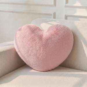 Peut inclure: Un coussin en forme de cœur rose tendre. Le coussin moelleux est fait d'un matériau doux et repose sur un canapé blanc. La forme du coussin est bien définie, avec des bords arrondis et un design symétrique.