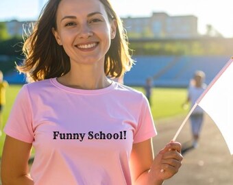 May include: A woman wearing a pink t-shirt with the text "Funny School!" printed in black. She is holding a white flag and smiling. The background includes a sports field and other people.