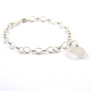 May include: A silver chain bracelet with a white sea glass charm. The bracelet is made of a delicate chain and the charm is a smooth, oval-shaped piece of sea glass.