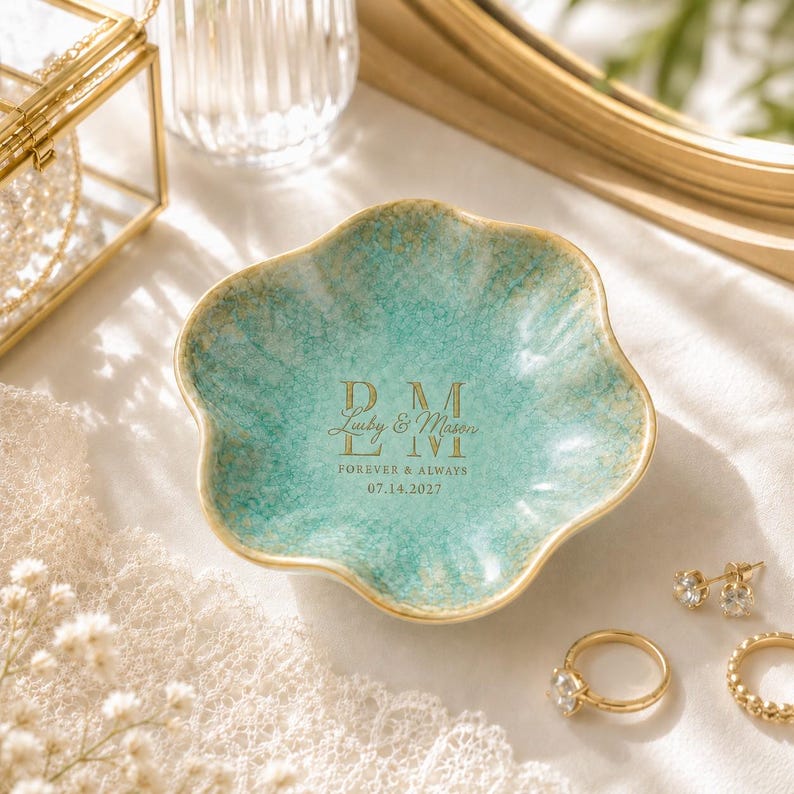 K&ouml;nnte beinhalten: Eine blumenf&ouml;rmige Schmuckschale mit einer t&uuml;rkisfarbenen und goldenen Craquel&eacute;-Glasur. In der Mitte befindet sich ein goldener Schriftzug mit "DM", "Luiby & Mason", "FOREVER & ALWAYS" und "07.14.2027". Die Schale hat einen gewellten Rand.