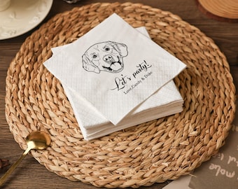 May include: White paper napkins featuring a black dog illustration and the text "Let's party! Love, Candy & Duke." The napkins are stacked on a woven placemat. A gold spoon and pinecone are visible in the background.