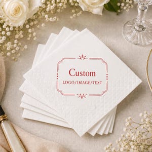 May include: A stack of square white paper napkins with a textured diamond pattern border. The centre features a red decorative frame with the text Custom LOGO/IMAGE/TEXT printed in red ink. The napkins are arranged in a layered, fanned-out stack.