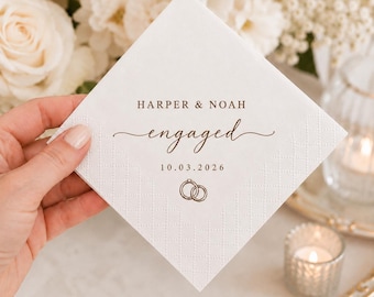 May include: A square white paper napkin with a textured diamond border pattern. The centre features brown printed text reading HARPER & NOAH, the word engaged in a script font, the date 10.03.2026, and a small icon of two interlocking rings.