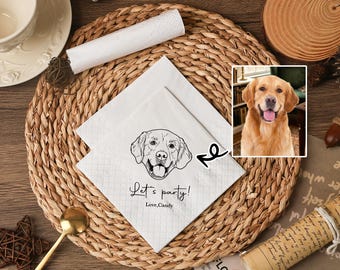 May include: White paper napkins featuring a black line drawing of a dog's face and the text "Let's party! Love, Candy". A small framed photo of a golden retriever is next to the napkins. The napkins are on a woven placemat.