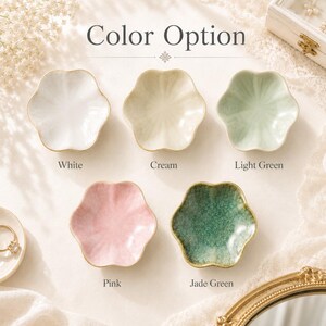 K&ouml;nnte beinhalten: F&uuml;nf blumenf&ouml;rmige Schmuckschalen aus Keramik in einer Rasteranordnung mit der Aufschrift Color Option. Die Schalen sind in Wei&szlig;, Creme, Hellgr&uuml;n, Rosa und Jadegr&uuml;n erh&auml;ltlich und haben einen gewellten Rand sowie einen goldenen Rand.