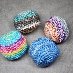 May include: Four handmade crochet balls in various colours. One is blue, another is a mix of blue, pink, and yellow. The third is a mix of purple, orange, and white, and the last is a mix of green, brown, and white.