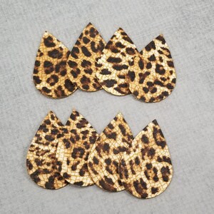 K&ouml;nnte beinhalten: Acht tropfenf&ouml;rmige Ohrringrohlinge mit Leopardenmuster. Die Ohrringe sind braun und beige mit dunkelbraunen Flecken. Die Rohlinge sind in zwei Reihen zu je vier St&uuml;ck auf einer grauen Oberfl&auml;che angeordnet.