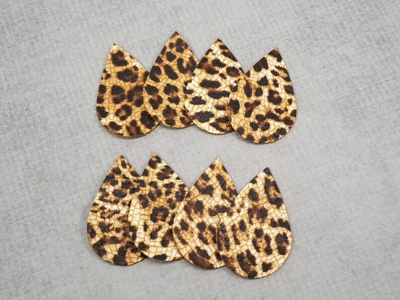 K&ouml;nnte beinhalten: Acht tropfenf&ouml;rmige Ohrringrohlinge mit Leopardenmuster. Die Ohrringe sind braun und beige mit dunkelbraunen Flecken. Die Rohlinge sind in zwei Reihen zu je vier St&uuml;ck auf einer grauen Oberfl&auml;che angeordnet.