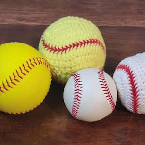 May include: Four baseballs and softballs are displayed. A bright yellow softball with red stitching is next to a white baseball with red stitching. A yellow crocheted softball and a white crocheted baseball are also shown.
