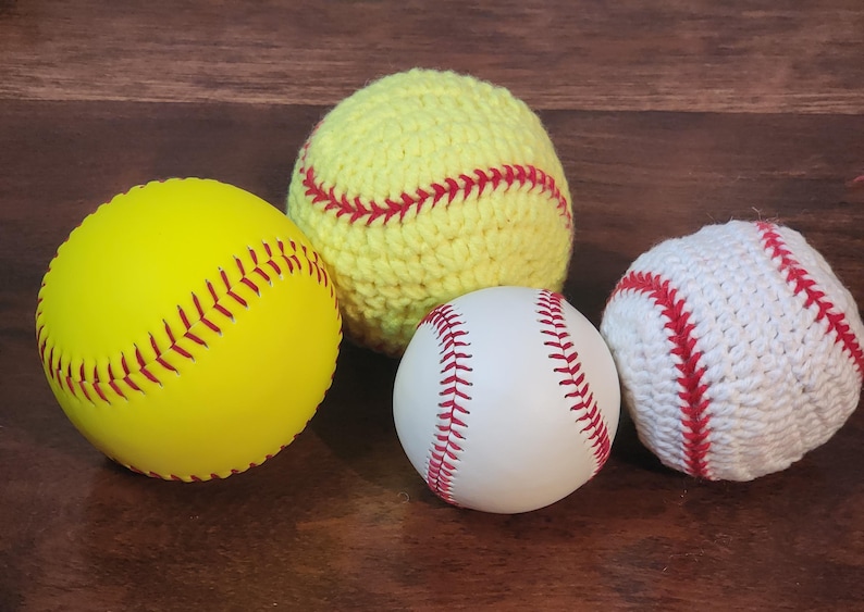 May include: Four baseballs and softballs are displayed. A bright yellow softball with red stitching is next to a white baseball with red stitching. A yellow crocheted softball and a white crocheted baseball are also shown.