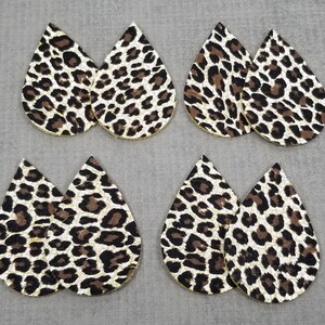 May include: Six teardrop-shaped earrings with a leopard print pattern. The earrings are made of faux leather and have a gold glitter finish.