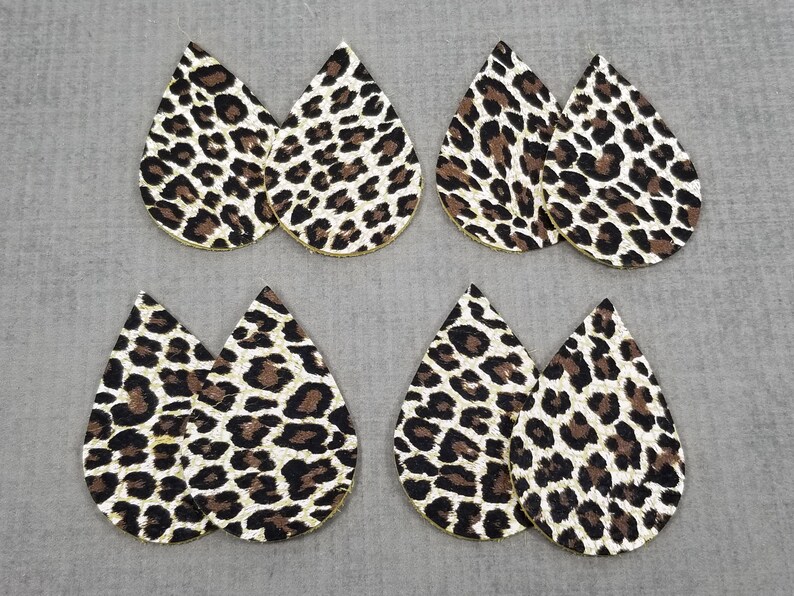 May include: Six teardrop-shaped earrings with a leopard print pattern. The earrings are made of faux leather and have a gold glitter finish.