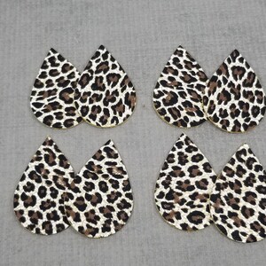 May include: Six teardrop-shaped leather earrings with a leopard print pattern. The earrings are white with black and brown spots.
