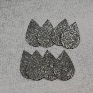 May include: Eight silver teardrop-shaped earrings with a textured, woven pattern. The earrings are arranged in two groups of four on a gray surface. These lightweight earrings are perfect for everyday wear.