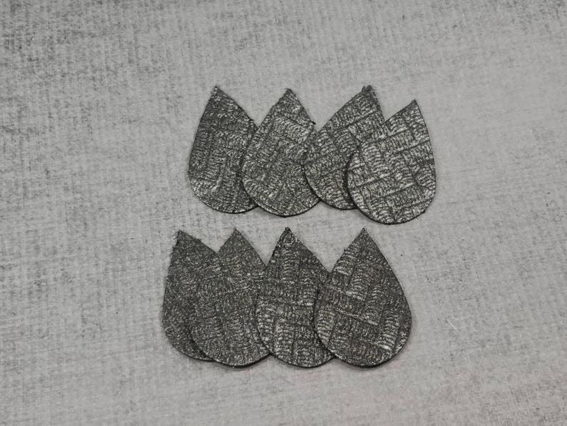 May include: Eight silver teardrop-shaped earrings with a textured, woven pattern. The earrings are arranged in two groups of four on a gray surface. These lightweight earrings are perfect for everyday wear.