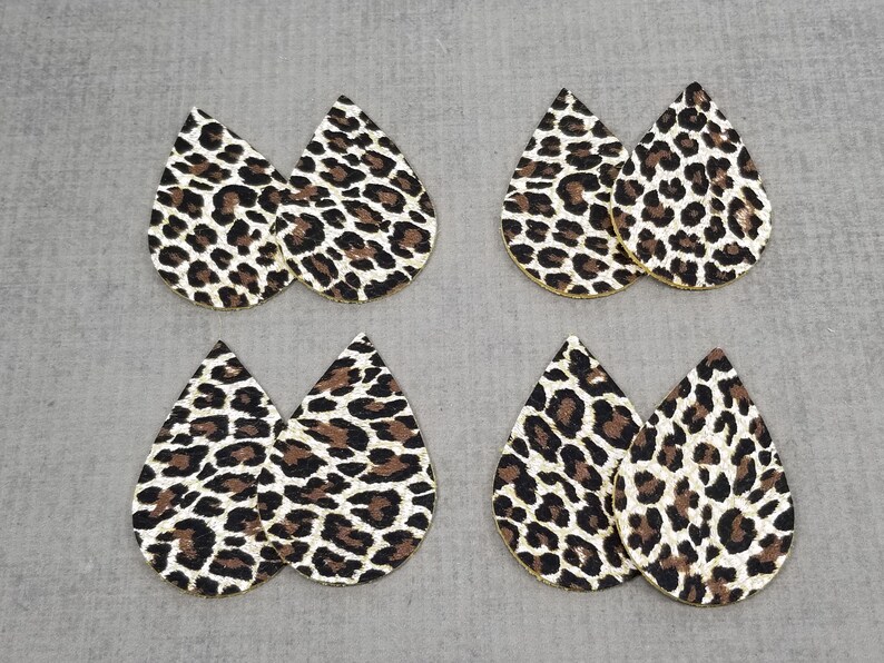 May include: Six pairs of leopard print teardrop shaped earrings. The earrings are made of faux leather and have a gold glitter finish.