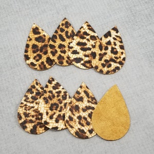 K&ouml;nnte beinhalten: Eine Sammlung tropfenf&ouml;rmiger Ohrring-Ausschnitte. Die nach vorne gerichteten Ausschnitte weisen ein tan- und braunes Leopardenmuster auf. Ein Ausschnitt wird mit der tanfarbenen Wildlederr&uuml;ckseite gezeigt. Die Ohrringe sind auf einer grauen Oberfl&auml;che angeordnet.