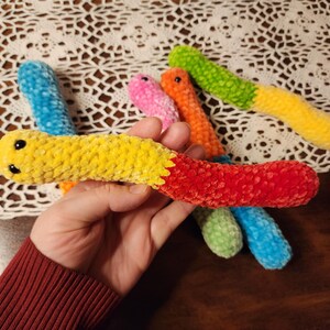 May include: A set of six colorful crocheted worm toys. The worms are made of soft, fuzzy yarn and have black eyes. The colors of the worms are blue, green, yellow, orange, pink, and red.