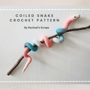 May include: A crocheted snake in pink, white, and blue colors is coiled around a branch. The snake has a small, white eye. The image includes the text "COILED SNAKE CROCHET PATTERN By Rachael's Scraps".
