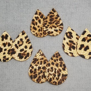 K&ouml;nnte beinhalten: Sechs Paar tropfenf&ouml;rmige Ohrring-Ausschnitte aus Kunstleder. Die Ausschnitte haben einen beigefarbenen Hintergrund mit braunen Leopardenflecken. Die Ohrringe sind auf einer grauen Oberfl&auml;che angeordnet.