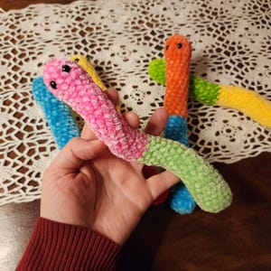 May include: Four colorful crocheted worm toys. The worms are pink, blue, green, and orange. They are all about 10 inches long and have a fuzzy texture.