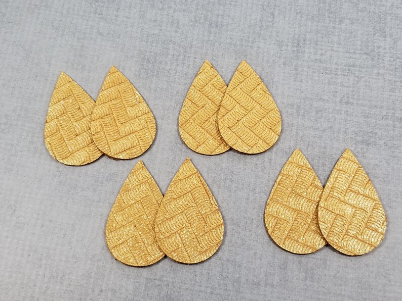 May include: Six teardrop-shaped, textured, golden-yellow leather earring blanks. Each earring blank has a woven pattern. The blanks are arranged on a light gray surface.