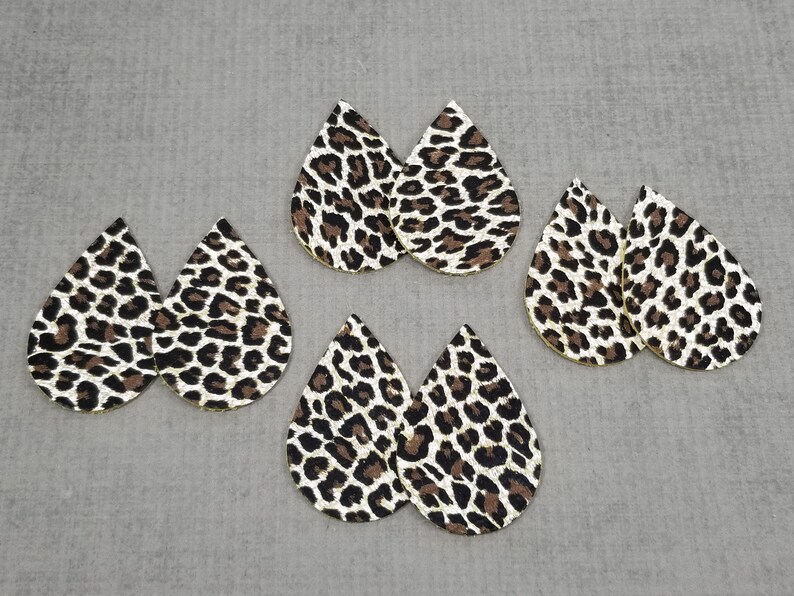 May include: Six teardrop-shaped earrings with a leopard print pattern. The earrings are made of faux leather and have a gold glitter finish.