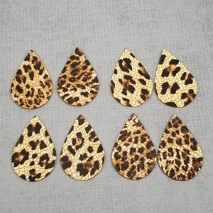 K&ouml;nnte beinhalten: Acht tropfenf&ouml;rmige Lederst&uuml;cke mit Leopardenmuster. Die St&uuml;cke sind beige mit braunen Flecken und auf einer grauen Oberfl&auml;che angeordnet. Diese St&uuml;cke sind wahrscheinlich f&uuml;r die Herstellung von Ohrringen oder anderen Schmuckst&uuml;cken bestimmt.