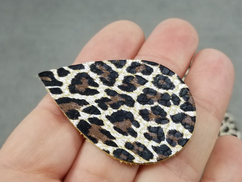 May include: A teardrop-shaped piece of leather with a brown, black, and white leopard print pattern.