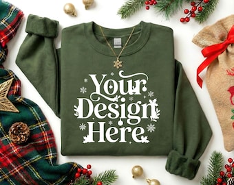 May include: An olive green sweatshirt with the text "Your Design Here" in white, surrounded by snowflakes. A gold necklace with a snowflake pendant is on the sweatshirt. The image is decorated with Christmas ornaments and greenery.