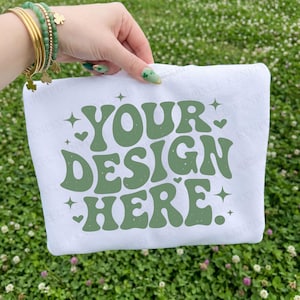 Könnte beinhalten: Ein weißes Sweatshirt mit dem grünen Text "YOUR DESIGN HERE", umgeben von Sternen und Herzen. Das Sweatshirt wird vor einem Hintergrund aus grünem Gras präsentiert.