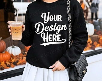 May include: A black sweatshirt with the text "Your Design Here" in white script. The person is holding a clear plastic cup with iced coffee. A black quilted purse hangs from the shoulder. The person is wearing a white pleated skirt.