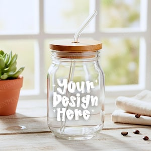 May include: A clear glass jar with a wooden lid and a glass straw. The jar has the text "Your Design Here" in white. The jar is on a wooden surface with a small potted plant and rolled white towels in the background.