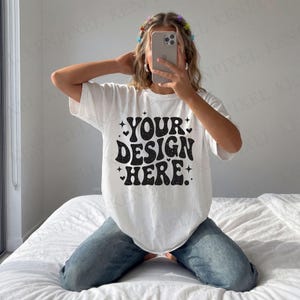 May include: White t-shirt with the text "YOUR DESIGN HERE" in a black, retro font. The design includes stars and hearts. The model is wearing blue jeans.